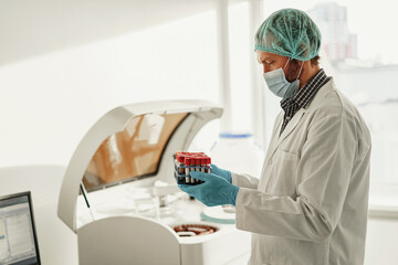 Scientist in uniform and mask holding test tubes at laboratory. Medicine and research in chemistry