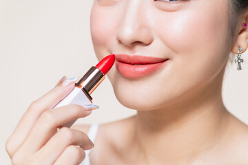 Young woman applying lipstick on beige