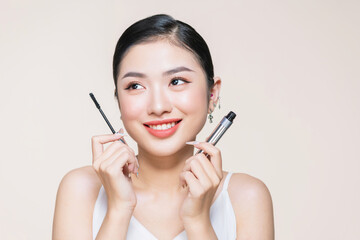 Beautiful asian young woman holding mascara and smiling on purple studio background,