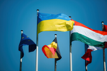 The Ukrainian flag waves proudly next to the European Union flag and other EU country flags, set against a clear, peaceful blue sky