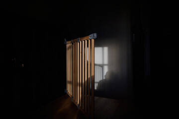 A morning scene featuring a safety baby gate open near a staircase, bathed in sunlight, with a whasto on the adjacent wall