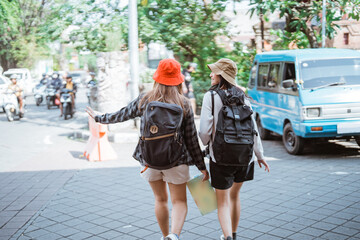 back view of two backpacker girls walking on the side of the road carrying a map while traveling