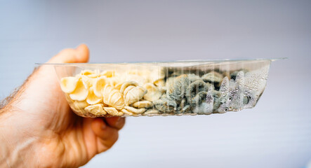 A male hand is holding a package of perished pasta, where half of the contents are still good, while the other half is covered with mold