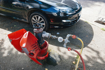 hydrant in full operation near a sleek black car. This juxtaposition of utility and modernity highlights the importance of emergency services in urban settings.