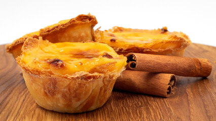Three Pastel de nata or Portuguese egg tart and cinnamon sticks on a wooden brown background. Pastel de Belem is a small dessert, a cup-shaped pastry made from puff pastry with custard.