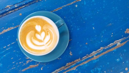 Top view of hot vanilla coffee latte and heart shaped latte art in blue glass with blue wooden...