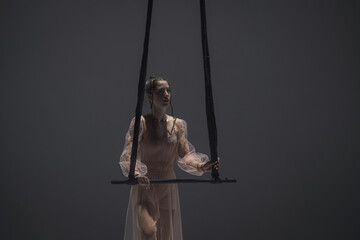 Aerial gymnast girl holding acrobatic trapeze on dark background of studio. Acrobatic athlete...