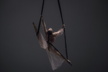 Girl aerial gymnast demonstrates stretching in twine on acrobatic trapeze. Acrobatic athlete...