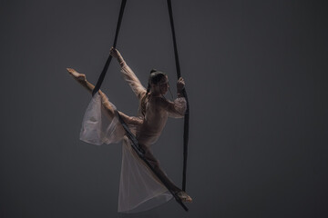 Girl aerial gymnast demonstrates stretching in twine on acrobatic trapeze. Acrobatic athlete...