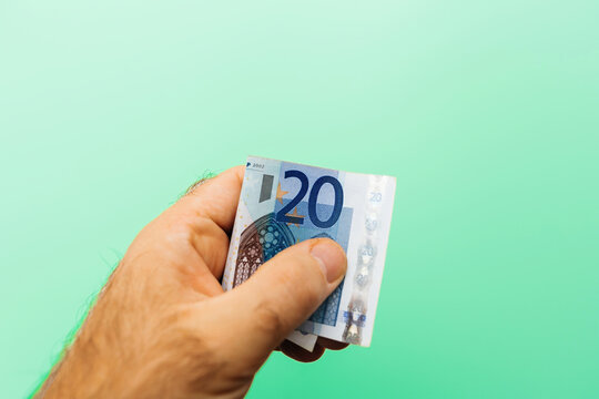 Male hand holding a 20 Euro bill on a green light background, symbolizing the concept of generosity, giving, and donation