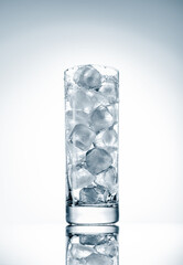 A tall transparent glass cup filled with natural ice cubes on a light background, backlit, studio shot.