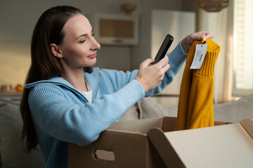 Brunette woman opens a parcel from an online store. A woman bought a mustard-colored sweater, scans...