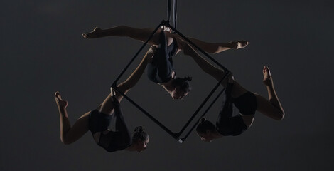 Trio of young female acrobats posing on a cube suspended at a height. Aerial gymnasts perform in...