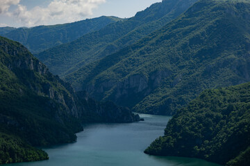 Fototapeta na wymiar Panoramic view of the bluish water of the Piva river in Montenegro, cutting through the green mountains under the cloudy skies