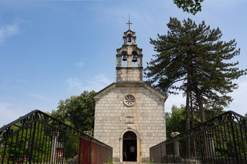 The Court Church in Ćipur (Castle Church) in Cetinje. Small bridge connecting to the stone church crowned with a cross and three bells, surrounded by trees under a blue sky