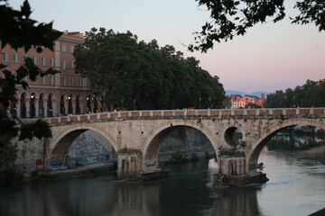 Fototapeta premium Rome, Italy - 06 26 2023: Ponte Sisto bridge spanning the river Tiber at dusk. Tourists gathered on it watching the pretty scene