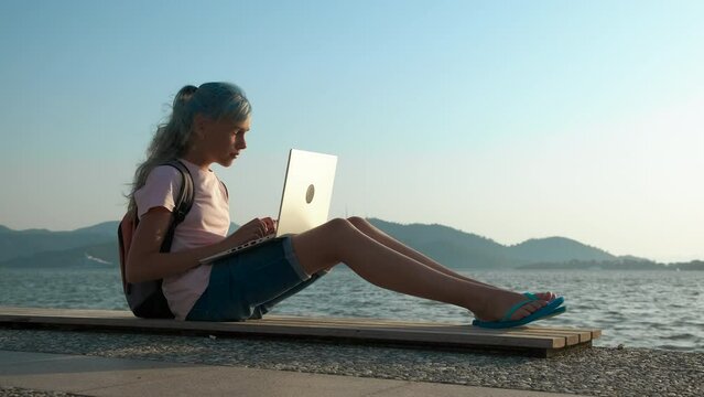 A young girl is resting with a laptop near the water