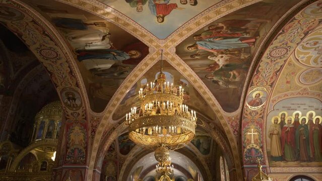 Vaulted arches of an Orthodox church adorned with frescoes and a gilded chandelier, reflecting a rich tapestry of religious art and history.