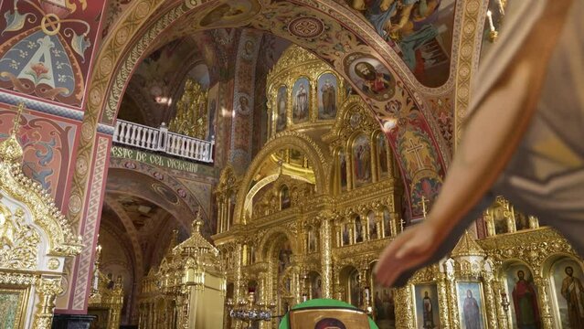 Inside an Orthodox church, a richly adorned altar with golden domes and religious icons stands amid vibrant frescoes.