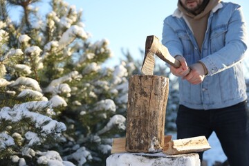 Man chopping wood with axe outdoors on winter day, closeup. Space for text