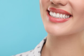 Woman with clean teeth smiling on light blue background, closeup. Space for text