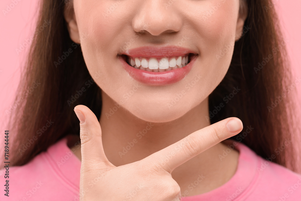 Wall mural beautiful woman showing her clean teeth and smiling on pink background, closeup