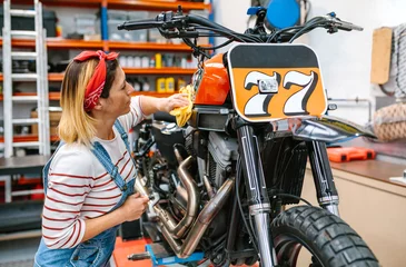 Photo sur Plexiglas Moto Concentrated mechanic woman cleaning fuel tank of custom motorcycle with a microfiber cloth and polish after repair on factory
