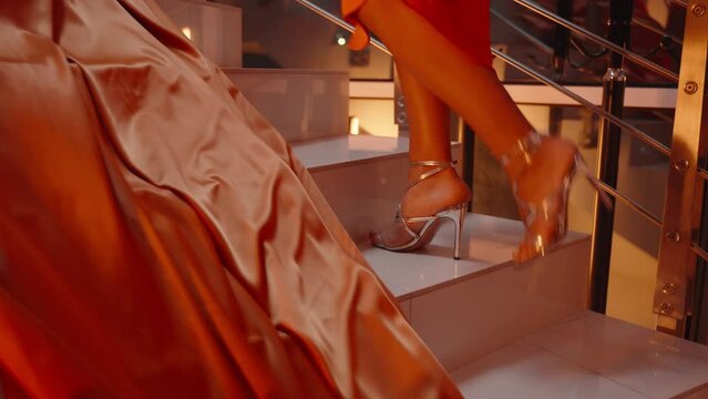 women ascending a set of stairs, portion of an orange dress. stairwell is modern with white steps and chrome railings, and an orange satin fabric cascades down steps
