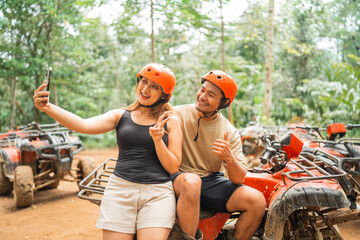 young asian couple taking selfie photos while sitting on the atv