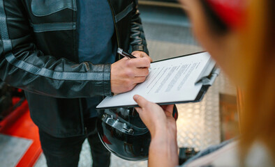 Unrecognizable biker man wearing leather jacket and holding helmet signing insurance policy to...