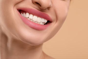 Woman with clean teeth smiling on beige background, closeup. Space for text