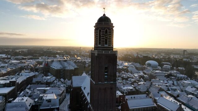 Zwolle Peperbus church tower rising up over the snow covered rooftops in the downtown district aerial drone view during a cold winter sunrise.