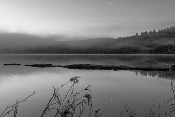 Crescent moon on misty loch in mono