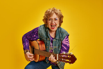 Portrait of elderly lady playing guitar with excited and joyful expression dressed denim attire,...
