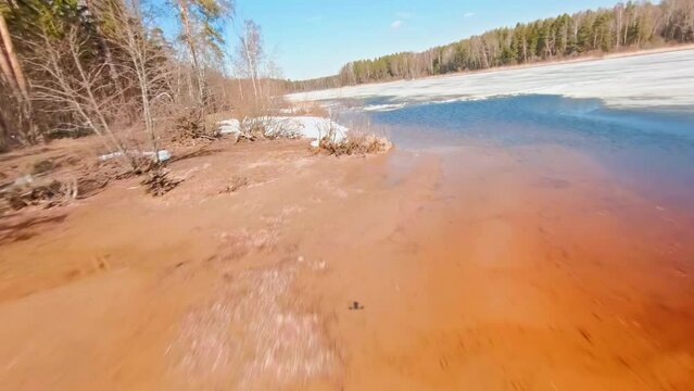 An amphibious vehicle traverses a swampy area, with spring ice formation all around. FPV Aerial Drone shot