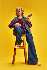 Full length portrait of laughing elderly woman lively playing ukulele, cross-legged on bar stool...