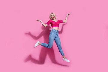Fototapeta na wymiar Full size photo of cute woman dressed knit top jeans pants jumping palms demonstrate objects empty space isolated on pink background