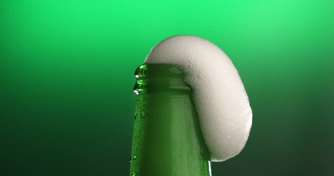 Super slow motion macro of fresh cold bio organic brewed beer in bottle with white bubbles foamy froth is going out isolated on bright green background at 1000 fps.