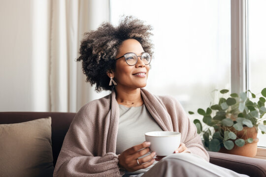 Satisfied middle aged woman drinking coffee relaxing on sofa at home. Smiling female enjoying resting sitting on couch in cozy living room. Portrait of relaxed female resting at home. 