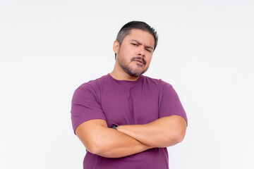 Portrait of a doubtful adult man with arms crossed, wearing a purple t-shirt, isolated on a white background. - obrazy, fototapety, plakaty