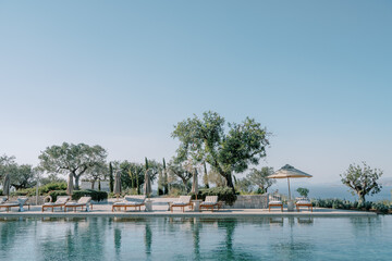 Fototapeta na wymiar Soft sun loungers under sun umbrellas stand by the pool. Hotel Amanzoe. Peloponnese, Greece