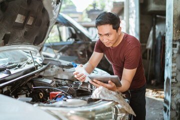 car mechanic using a laptop while holding a battery water bottle to maintain a car battery at a...