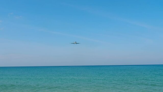 Civil plane approaching to land over the azure sea, bottom view. Airliner arrival on the island. Tourism and travel concept