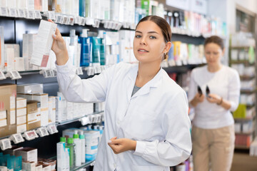 Young woman pharmacist distributes assortment of goods on counter in pharmacy