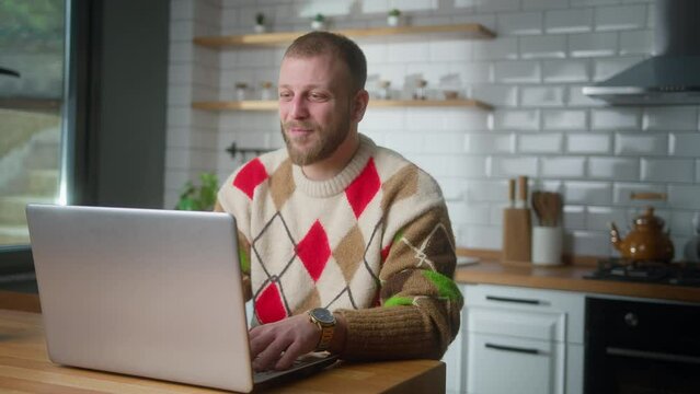 Smiling adult man sitting in the kitchen having video call conversation through using laptop computer. Share news, talk to family, enjoy webchat virtual meeting