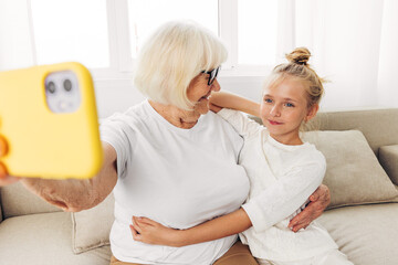 Fototapeta premium Child togetherness granddaughter grandmother phone smiling sofa family hugging selfie bonding