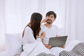 Happy asian man and woman using laptop sitting relaxed on a bed at home enjoy, Happy lover hug each other and smiling on the bed, Male and female couple concept.