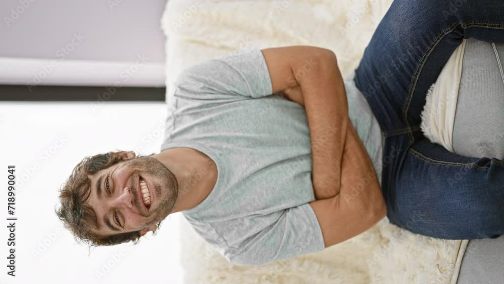 Poster Young, confident man sits joyfully on his cozy sofa with crossed arms, happiness oozing from his smile, looking right into the camera. makes trust look so stylish!