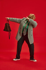 Feel young. Woman in smart casual, elegant outfit dancing hip-hop movement against red backdrop. Funny grandmother portrait. Concept of fashionable older adults, active seniors in modern life. Ad