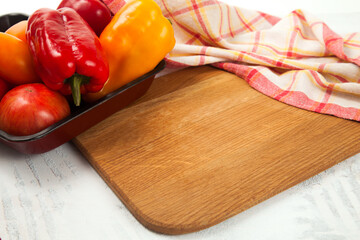 Cutting board with assort of different tomatoes and bell pepper on white wooden background..